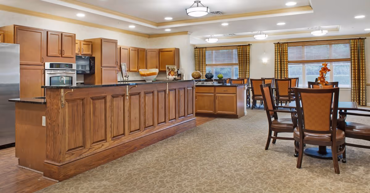 Bright communal dining area with a long wooden serving counter, kitchen cabinets, and multiple dining tables and chairs.
