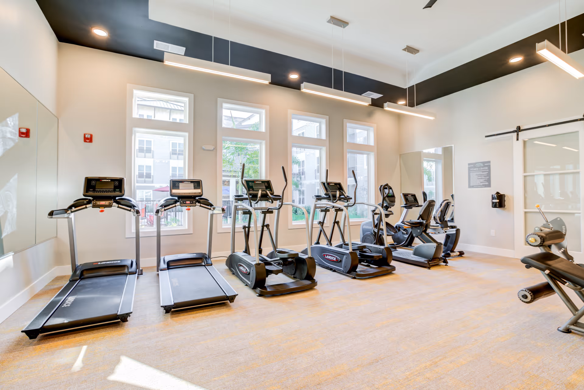 Bright fitness room with treadmills, ellipticals, and large windows.
