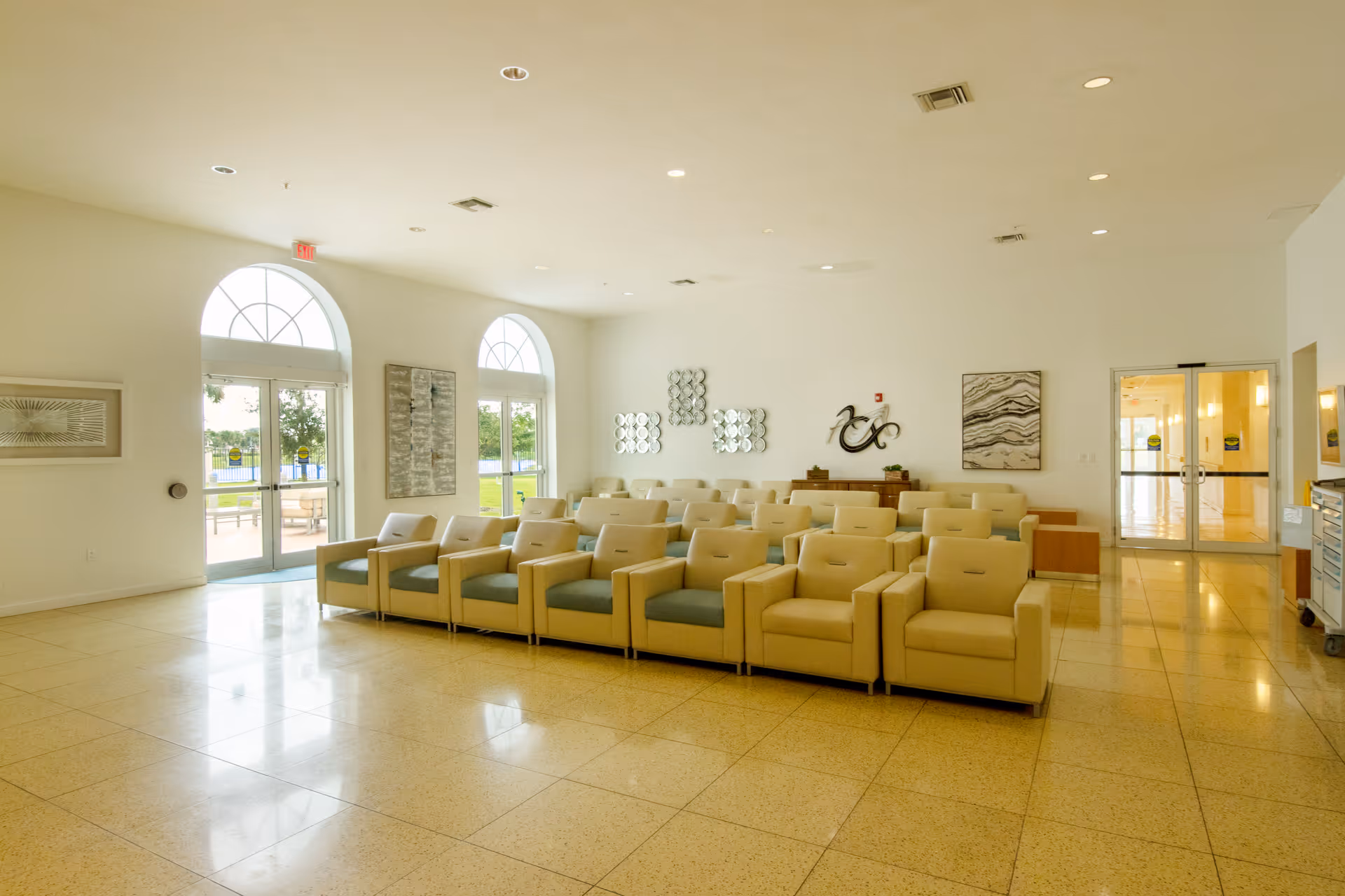 Bright, spacious common lounge with rows of beige armchairs, arched windows, and glass doors