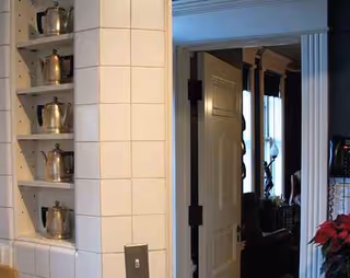 Doorway opens to a dim room; tiled wall shelves hold metal pitchers.