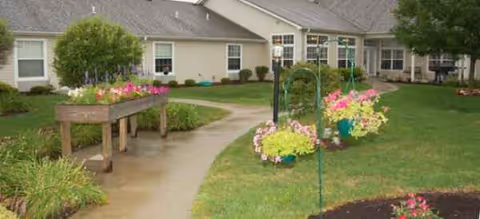 Pathway and lawn lead to Brookdale Greenville's front entrance with colorful planters and flowers.