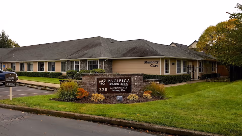 Single-story Pacifica Senior Living Memory Care building with a brick sign reading 'Pacifica Senior Living 320' and a landscaped lawn in front.