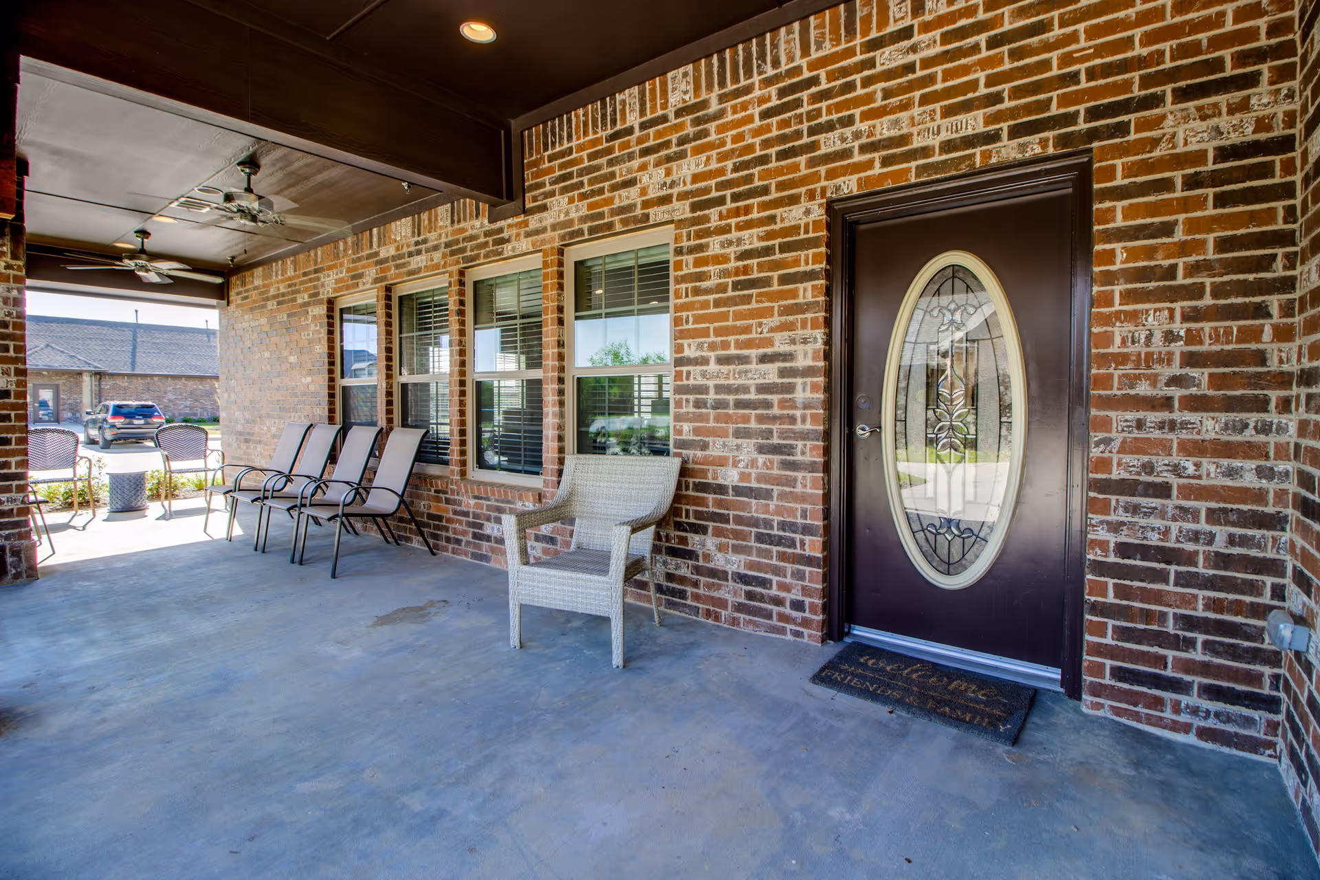 Covered brick front porch with several chairs and a decorative oval-glass entry door.