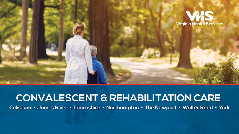 A healthcare worker in a white coat pushing an elderly person in a wheelchair along a tree-lined path in a park or garden setting during daytime.