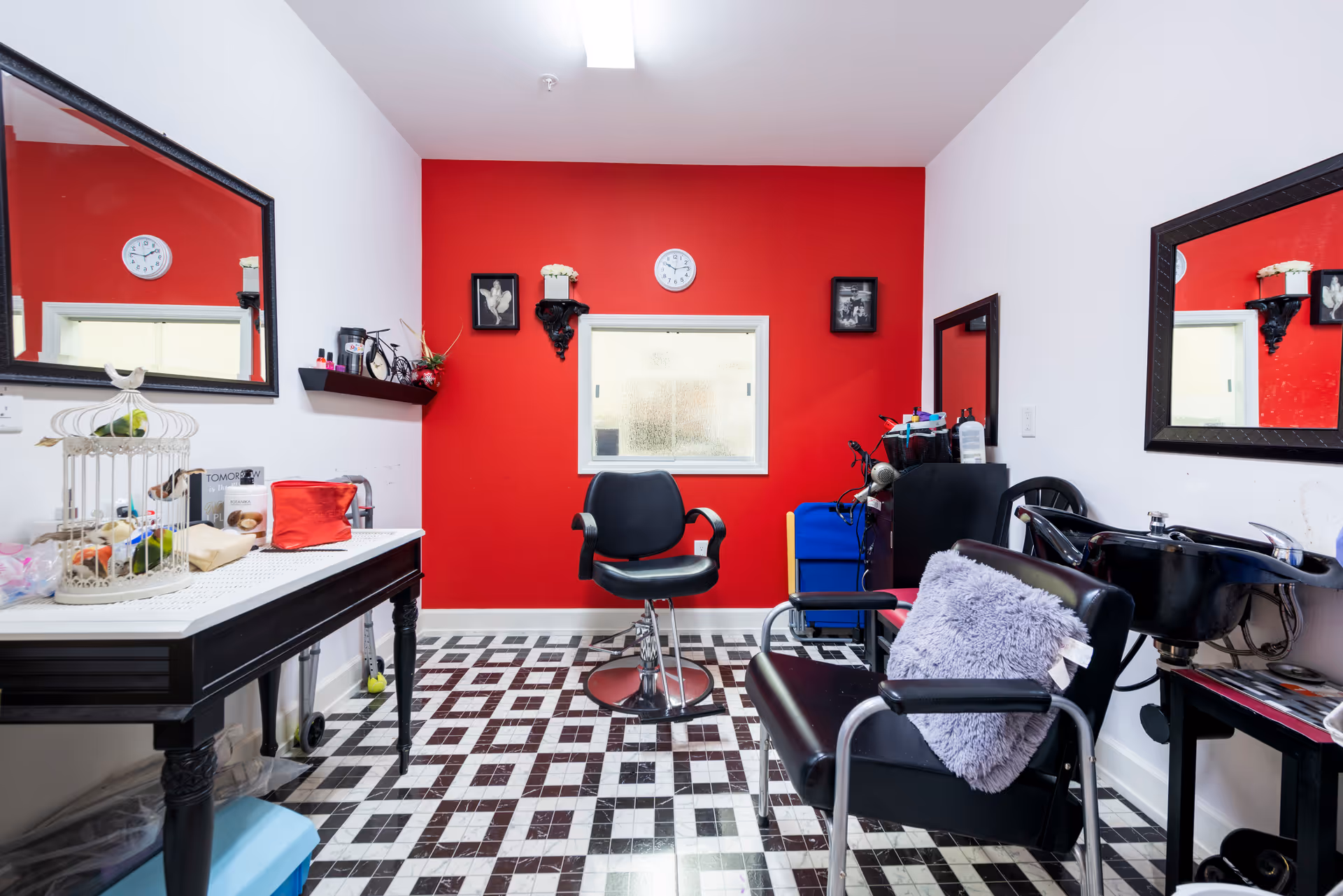 Salon-style interior with a red accent wall, styling chairs, mirrors, and a hair-wash sink.