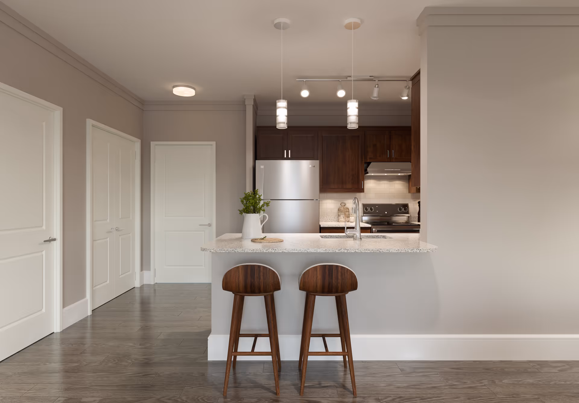 Modern kitchen area with a granite countertop island featuring two wooden bar stools. The kitchen has dark wood cabinets, a stainless steel refrigerator, an electric stove with a range hood, and a white subway tile backsplash. There are two pendant lights hanging above the island and a small plant in a white pitcher on the countertop. The floor is wood, and there are three white doors visible on the left side of the image.