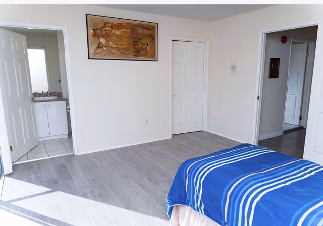 A bedroom in a senior living facility with a blue striped bed and doorway to bathroom.