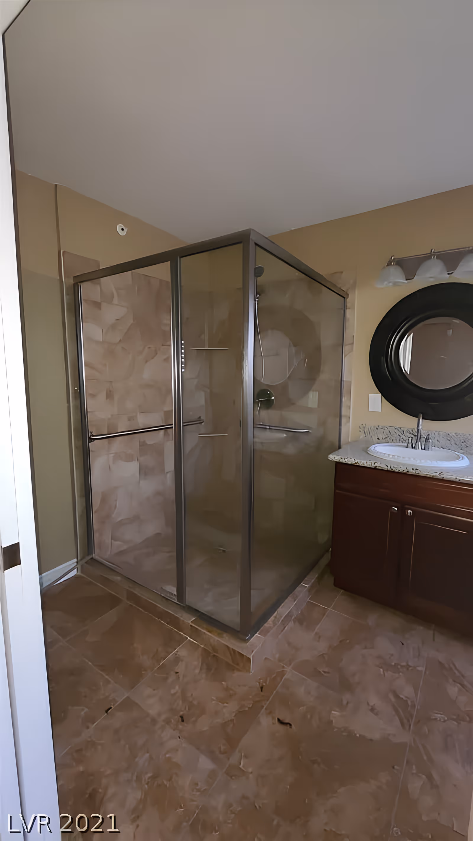 Glass-enclosed corner shower and a vanity with a round mirror in a bathroom.