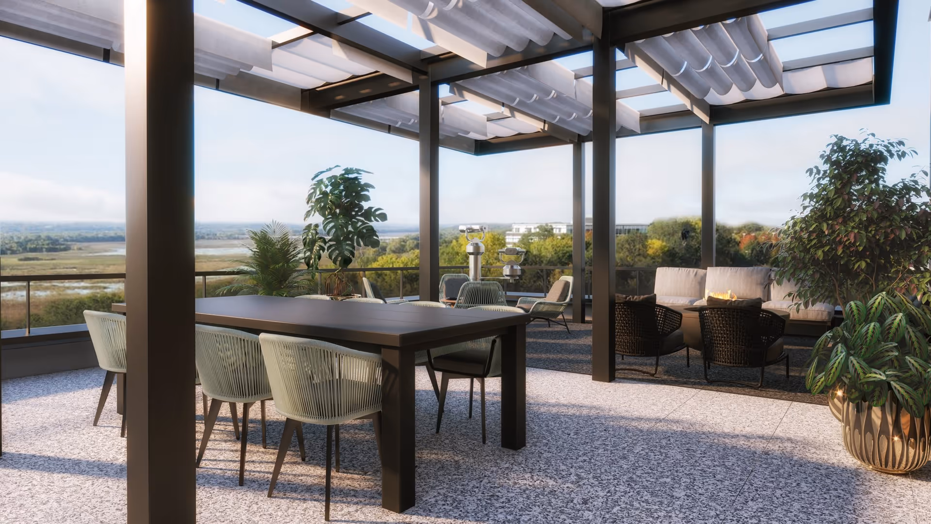 Outdoor patio area with a modern pergola overhead, featuring a dining table with six chairs and a seating area with cushioned chairs and a sofa around a fire pit. The space is decorated with potted plants and overlooks a scenic view of trees and water in the distance.