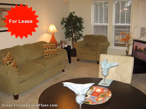 Living room with a sofa, armchair, round dining table set with napkins, TV, lamp and potted plant, with a red 'For Lease' starburst overlay.