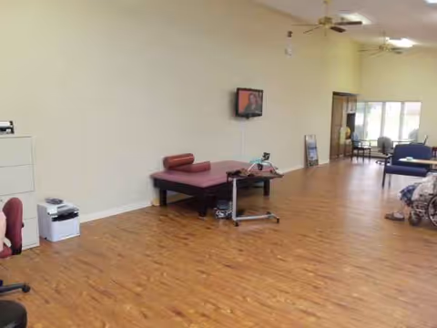 Wide interior room with a red examination bed, wall-mounted TV, and wooden flooring.