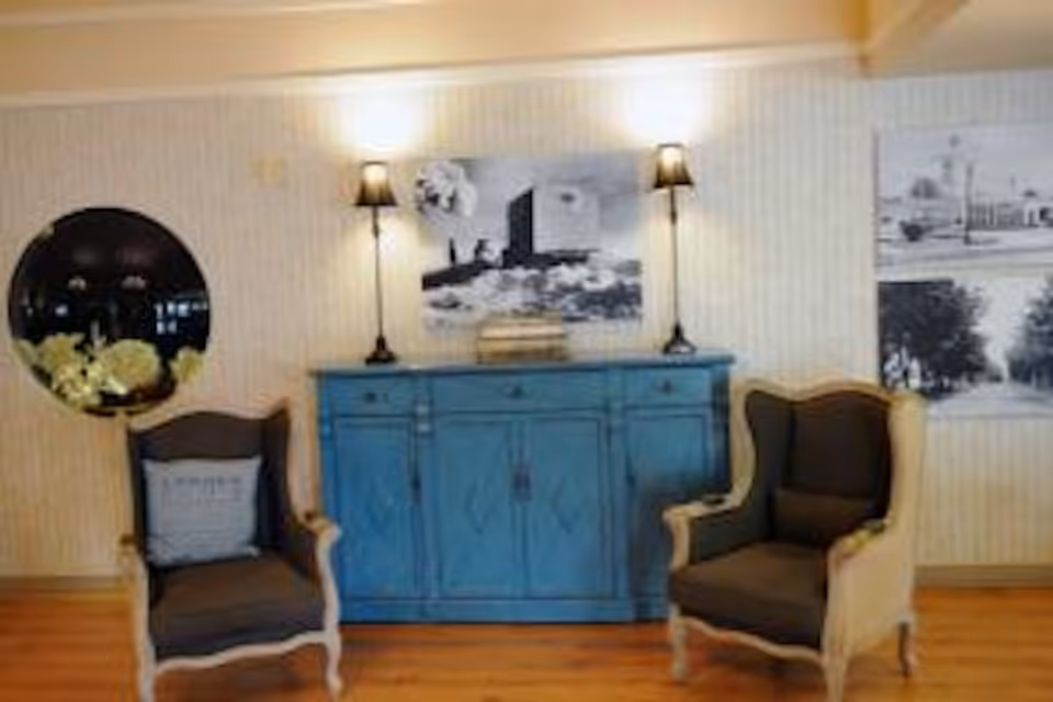 Two upholstered armchairs flank a blue sideboard topped with lamps and artwork in a cozy sitting area.