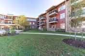 Courtyard lawn and walkway in front of a multi-story senior living building with balconies and trees.