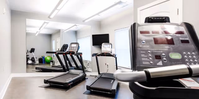 A small fitness room with treadmills, a mirror wall, and exercise equipment.