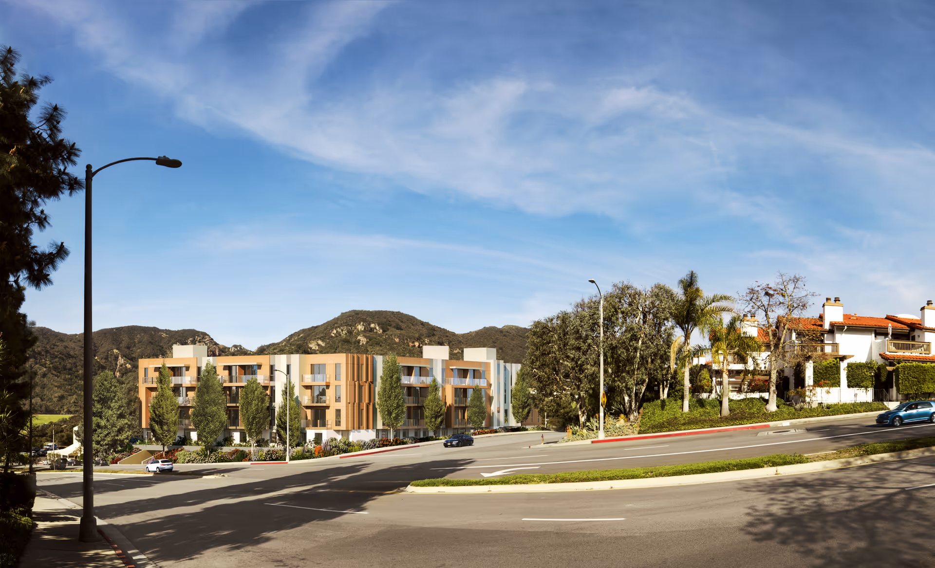 Street view of a modern three-story senior living building set against hills with trees, palm trees, and cars on the roadway.