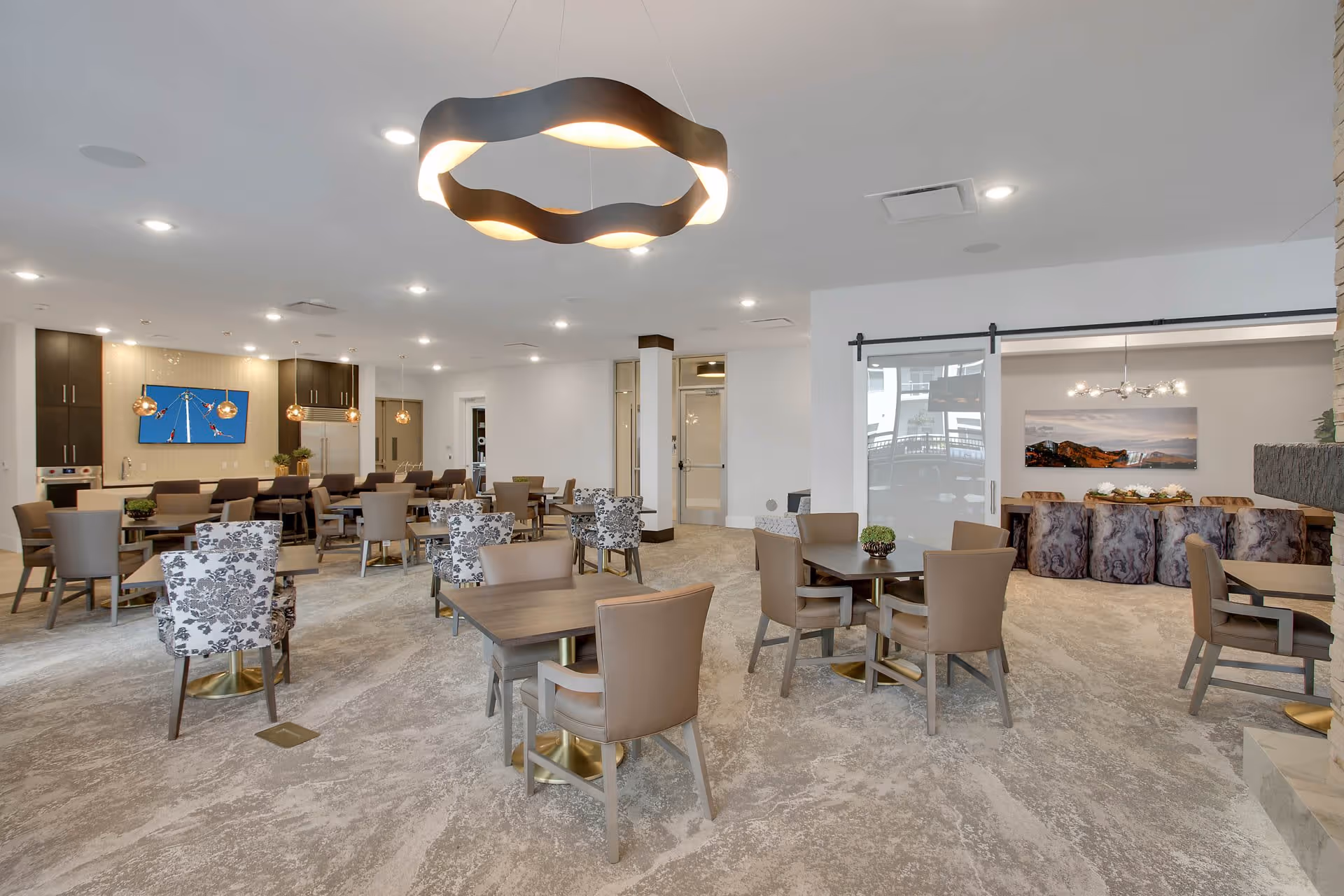 Spacious modern communal dining and lounge area with multiple tables and chairs, patterned armchairs, and contemporary lighting.