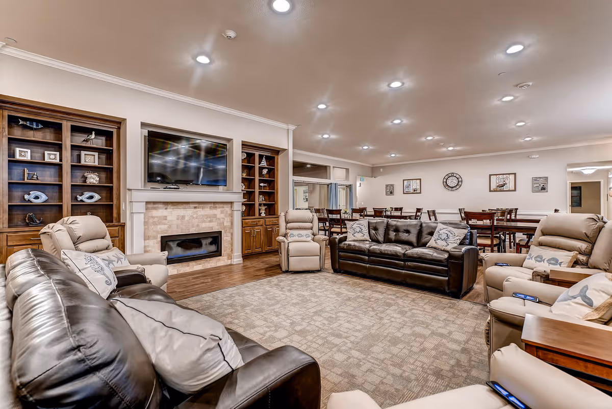Spacious senior living lounge with leather sofas, fireplace, TV, and dining area.