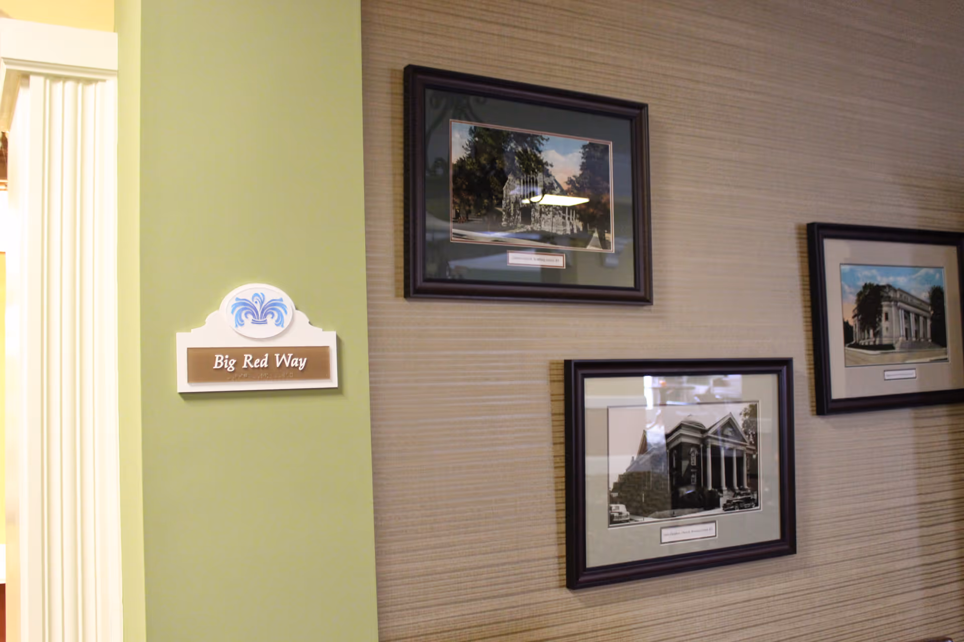 Interior hallway wall with framed pictures and a 'Big Red Way' sign on a green column.