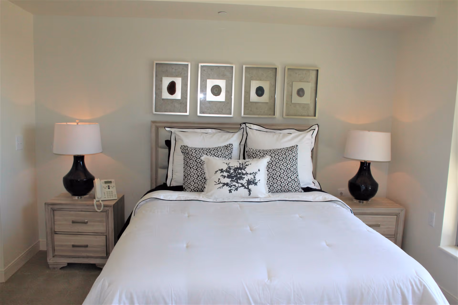Neat bedroom with a made double bed, decorative pillows, two nightstands with lamps, and framed art above the headboard.