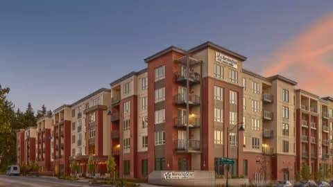 Front exterior of a multi-story senior living apartment building at dusk.