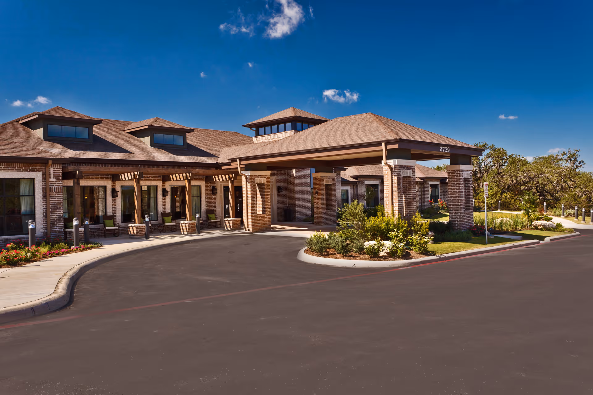 Exterior view of Adante assisted living facility showing a brick building with a covered entrance, large windows, and a driveway under a clear blue sky.
