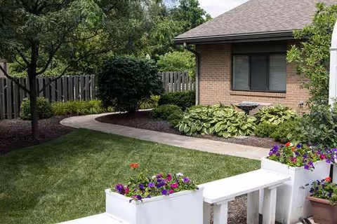 Exterior view of a brick building with a walkway, lawn, and colorful flowers.
