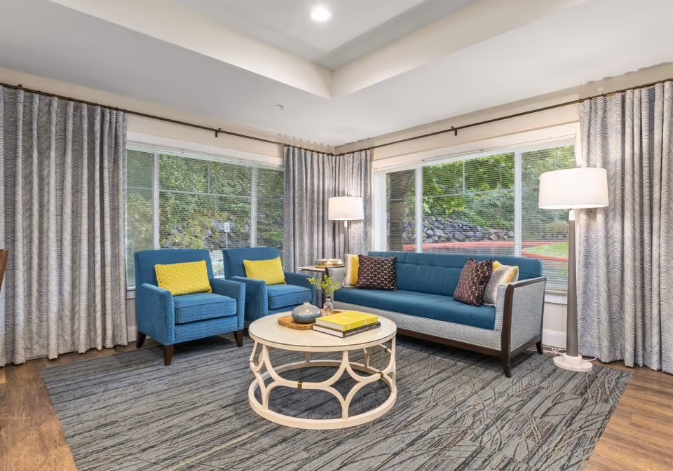 Bright seating area with a teal sofa, two matching armchairs, and a round coffee table in front of large windows.