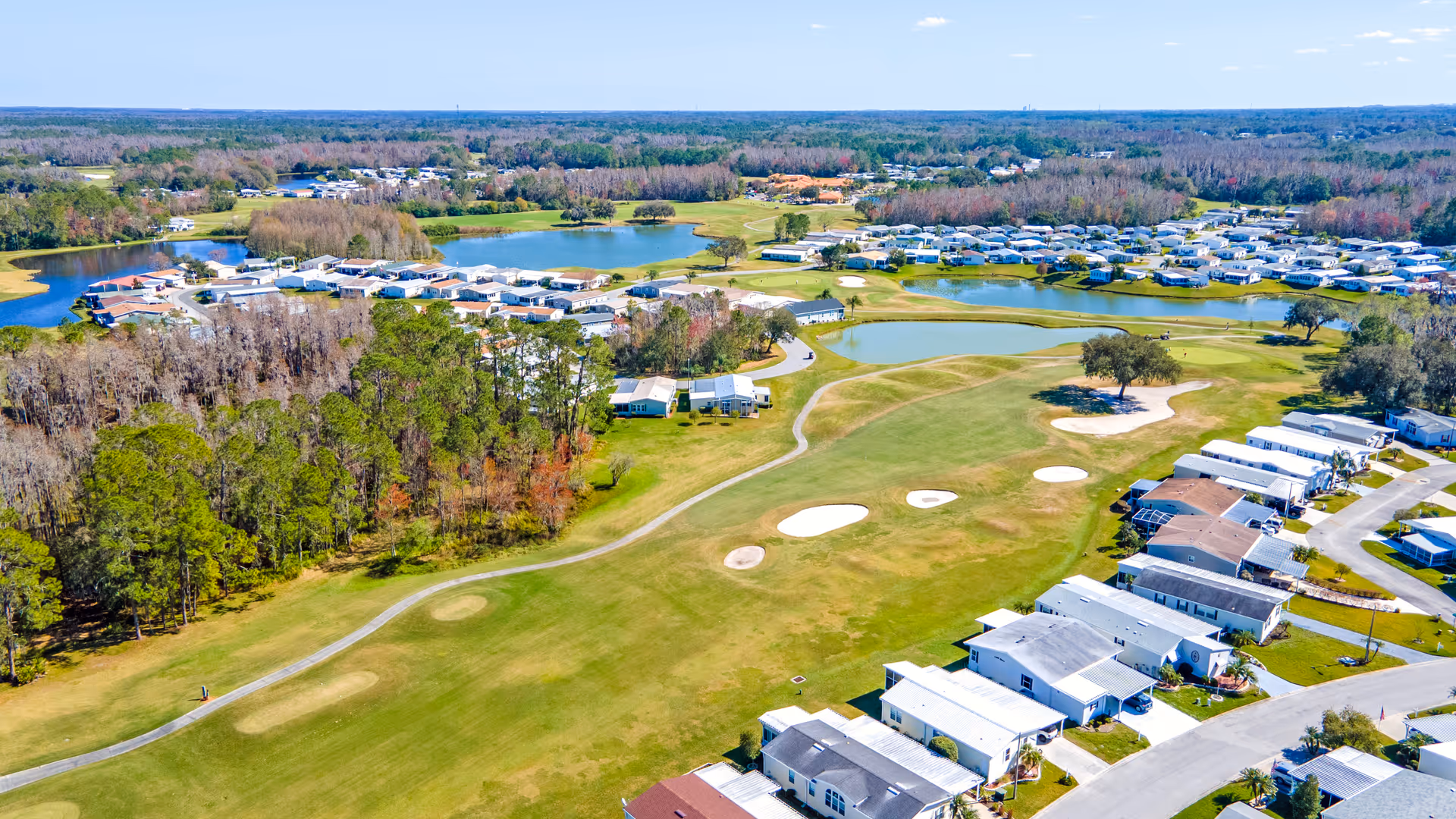 Aerial view of Cypress Lakes Village showing rows of homes beside a golf course with sand bunkers and ponds.