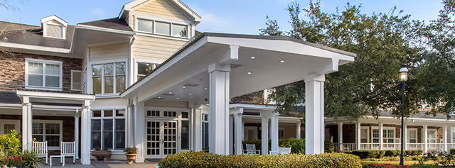 Brookdale Champions exterior with a covered entrance, columns, and seating under a porte-cochere.
