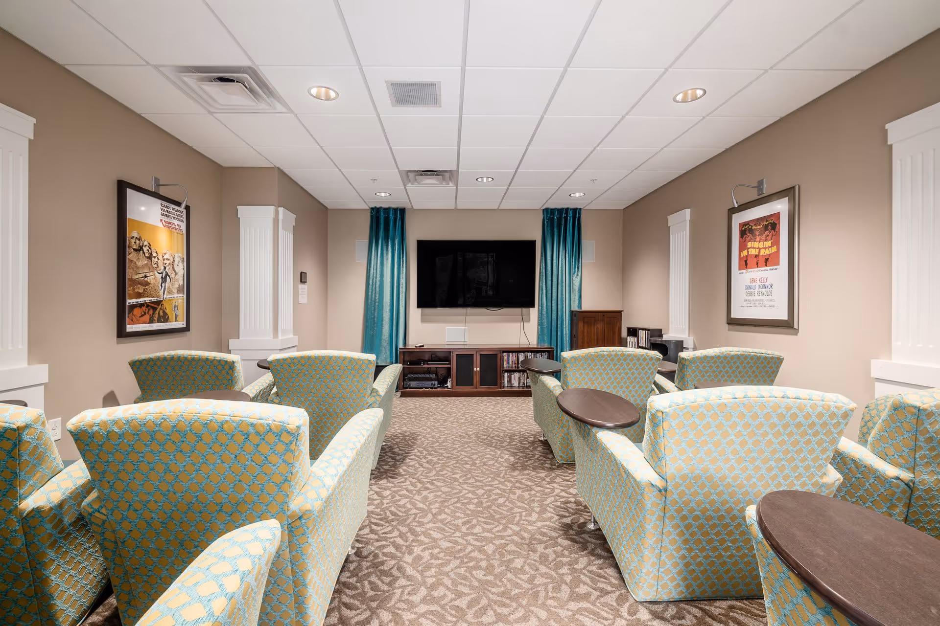 Small media room with patterned armchairs arranged facing a wall-mounted TV and framed posters.