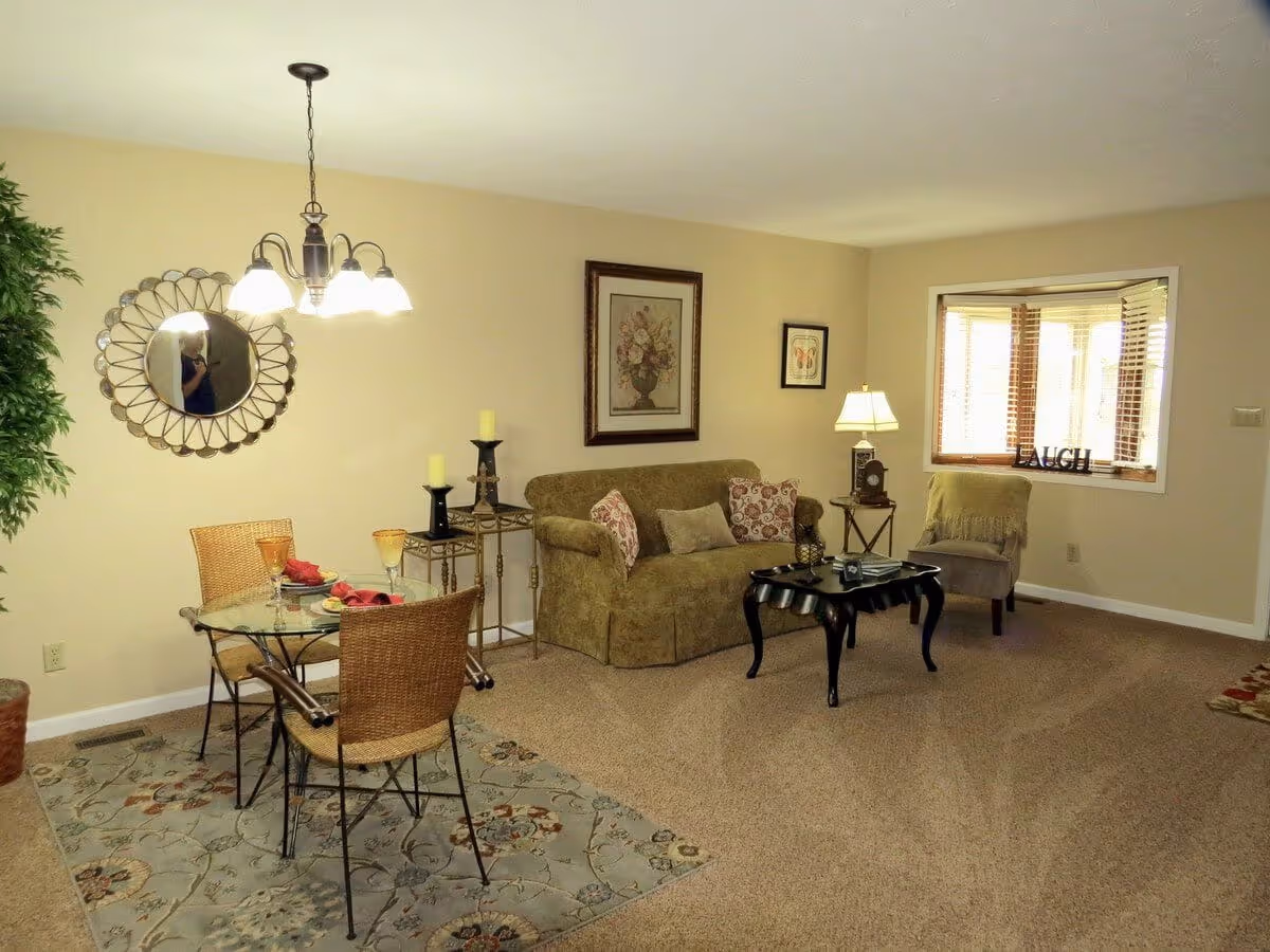 Cozy combined living and dining area with a glass dining table and wicker chairs, a sofa, coffee table, and a bay window.