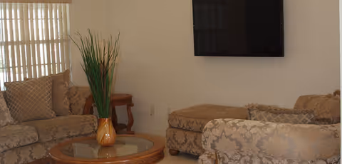 Cozy living room with beige patterned sofas, a glass coffee table, and a wall-mounted TV.