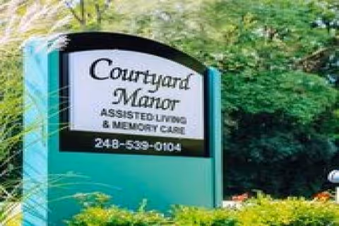Outdoor sign for Courtyard Manor Assisted Living & Memory Care amid greenery.