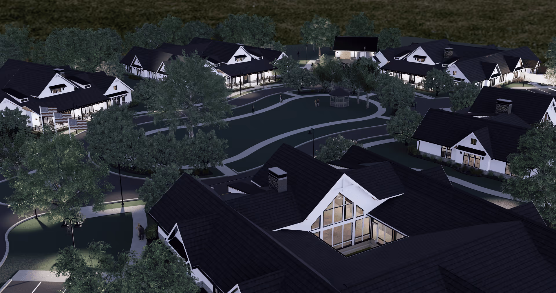 Aerial nighttime view of a senior living campus with multiple lit cottages, curving walkways, trees, and a central green with a gazebo.