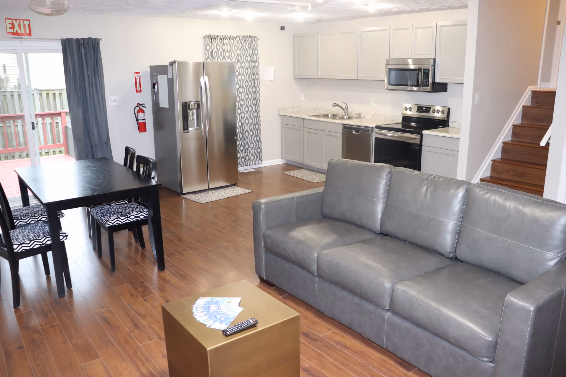 Open-plan living area with a gray leather sofa, dining table, and a kitchen with stainless steel appliances.