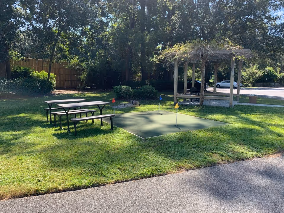Outdoor courtyard with a small putting green, picnic tables, and a wooden pergola.