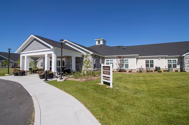 Exterior view of StoryPoint Chesterfield senior living facility showing a single-story building with a covered entrance, a well-maintained lawn, and a clear blue sky.