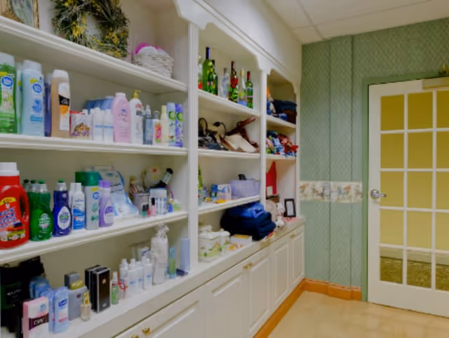 Built-in white shelves filled with toiletries, bottles, and folded linens in a small interior room with a glass-paneled door.