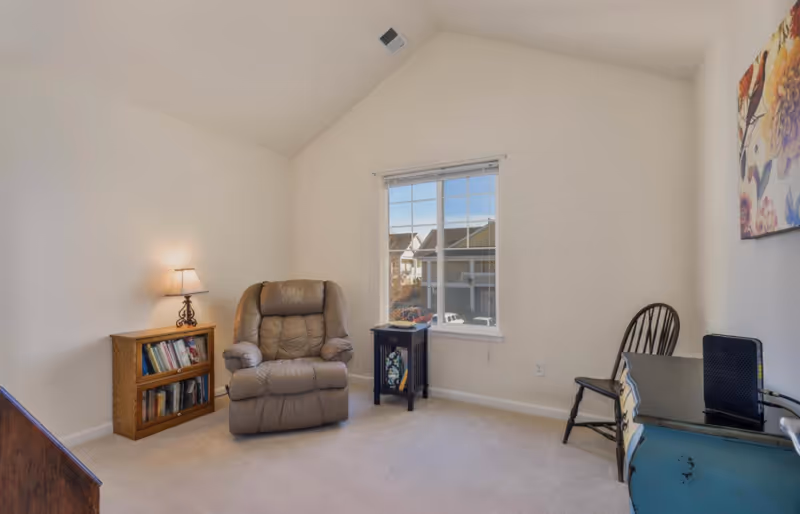 Bright small living room with a recliner, bookshelf, window, side table and desk with chair.
