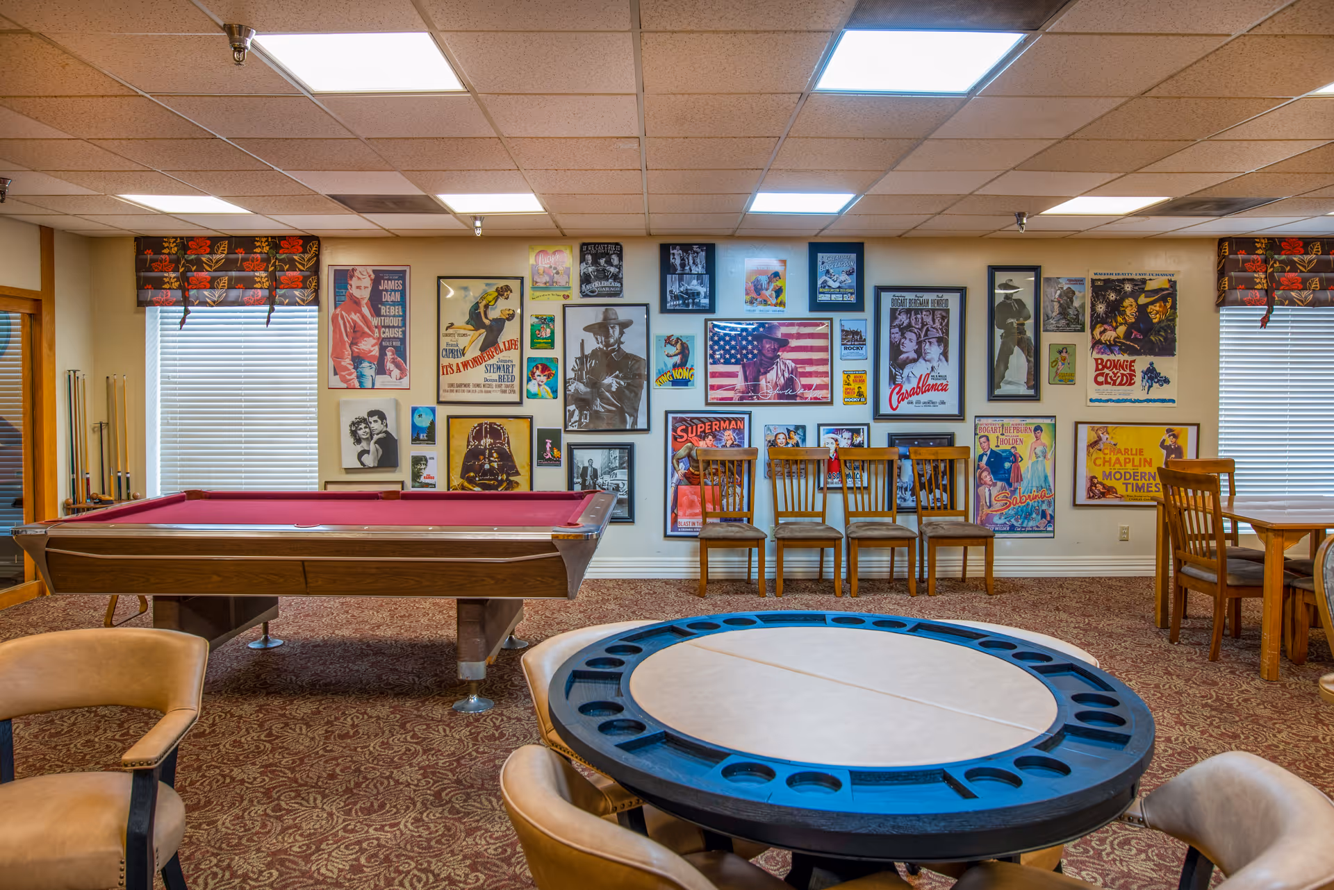 Game room with a red-felt pool table, round gaming table with cup holders, multiple chairs, and a wall covered in vintage movie posters.