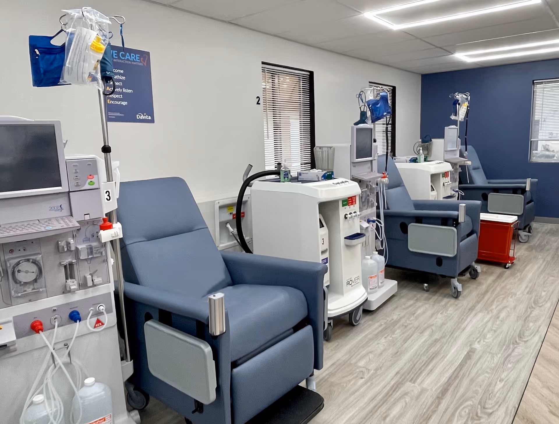 Row of blue dialysis chairs and medical machines arranged in a clinical treatment room.