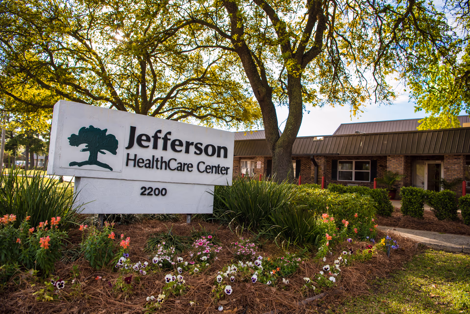 A landscaped entrance sign reading "Jefferson HealthCare Center 2200" in front of a single-story brick building and trees.