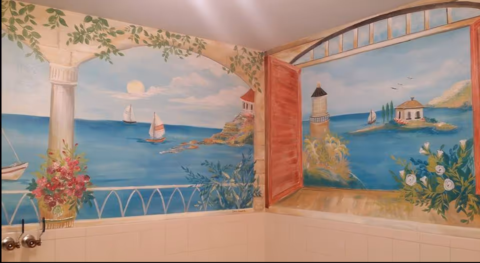 Painted wall mural of a seaside scene with sailboats, a lighthouse and open shutters above tiled bathroom walls and faucet handles.