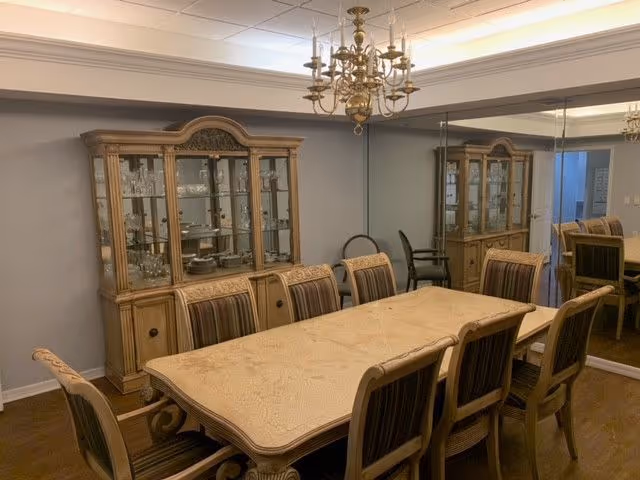 Formal dining room with a long wooden table, eight upholstered chairs, a china cabinet, a chandelier, and a mirrored wall.