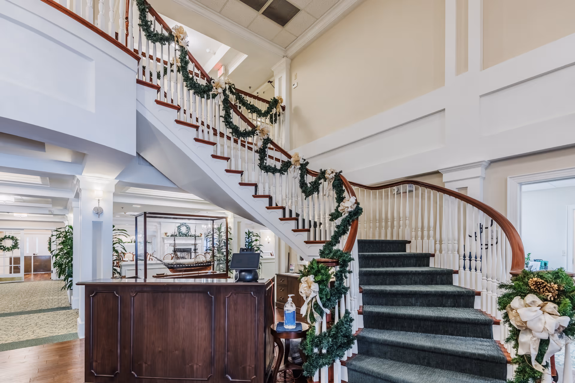 Lobby interior with a curved staircase decorated with garlands and a wooden reception desk.