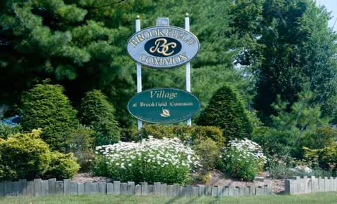 Outdoor sign for Village at Brookfield Common surrounded by greenery.