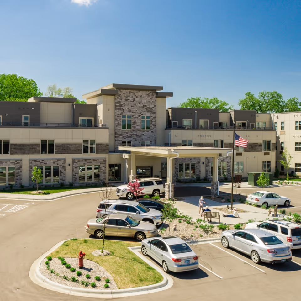 Front exterior of Havenwood of Minnetonka senior living building with covered entrance, parked cars, and an American flag.