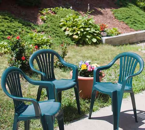 Patio with four teal plastic chairs and potted flowers in a garden.