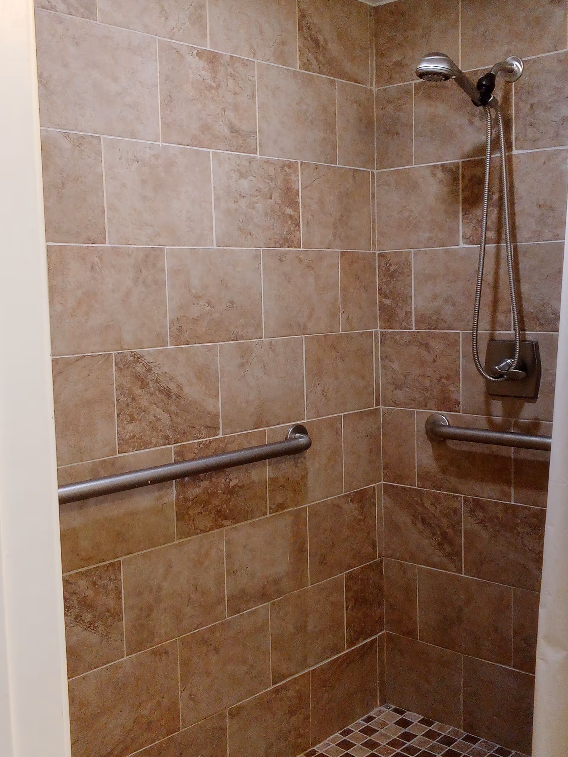 Accessible tiled shower with grab bars and a handheld shower head.