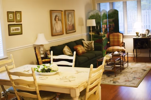 Cozy combined living and dining area with a wooden dining table in the foreground and a sofa, armchairs, and coffee table in the background.